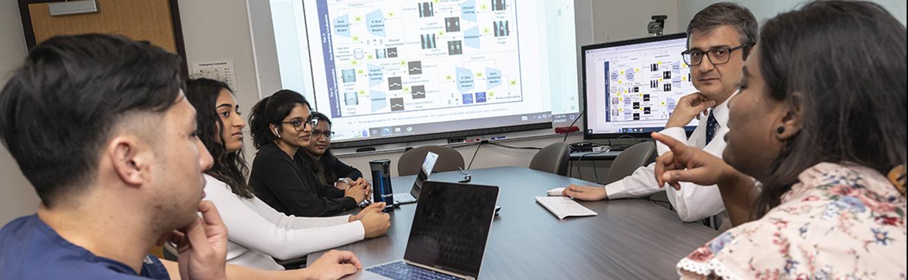 students and instructor meet around table in health informatics class